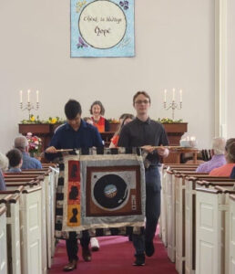Photo of two coming of age kids holding banners as they walk down the church aisle.