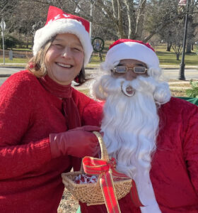 Rev. Lee in a santa hat holding a basket with red bow with Santa