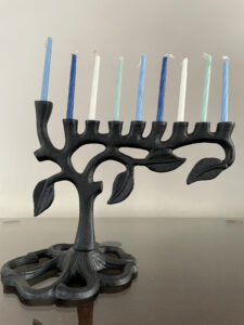 Photo of a black menorah, designed to look like a branching tree, with blue and white candles