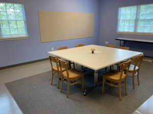 The Blue Room, used for classes and meetings, set up with center table surrounded by wooden chairs, two walls of window