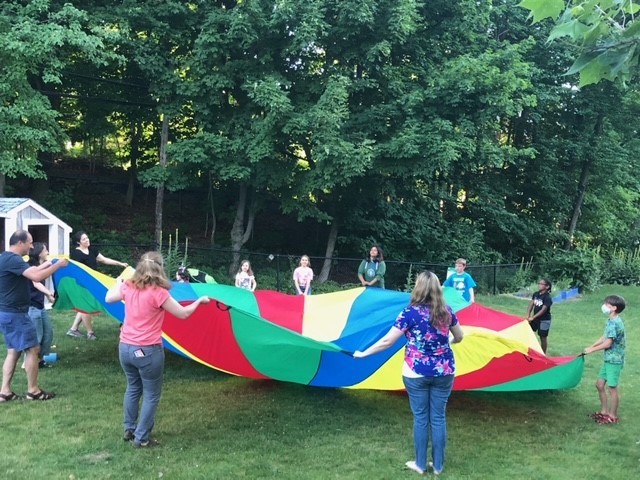 Children and adults play with a colorful parachute in the backyard garden