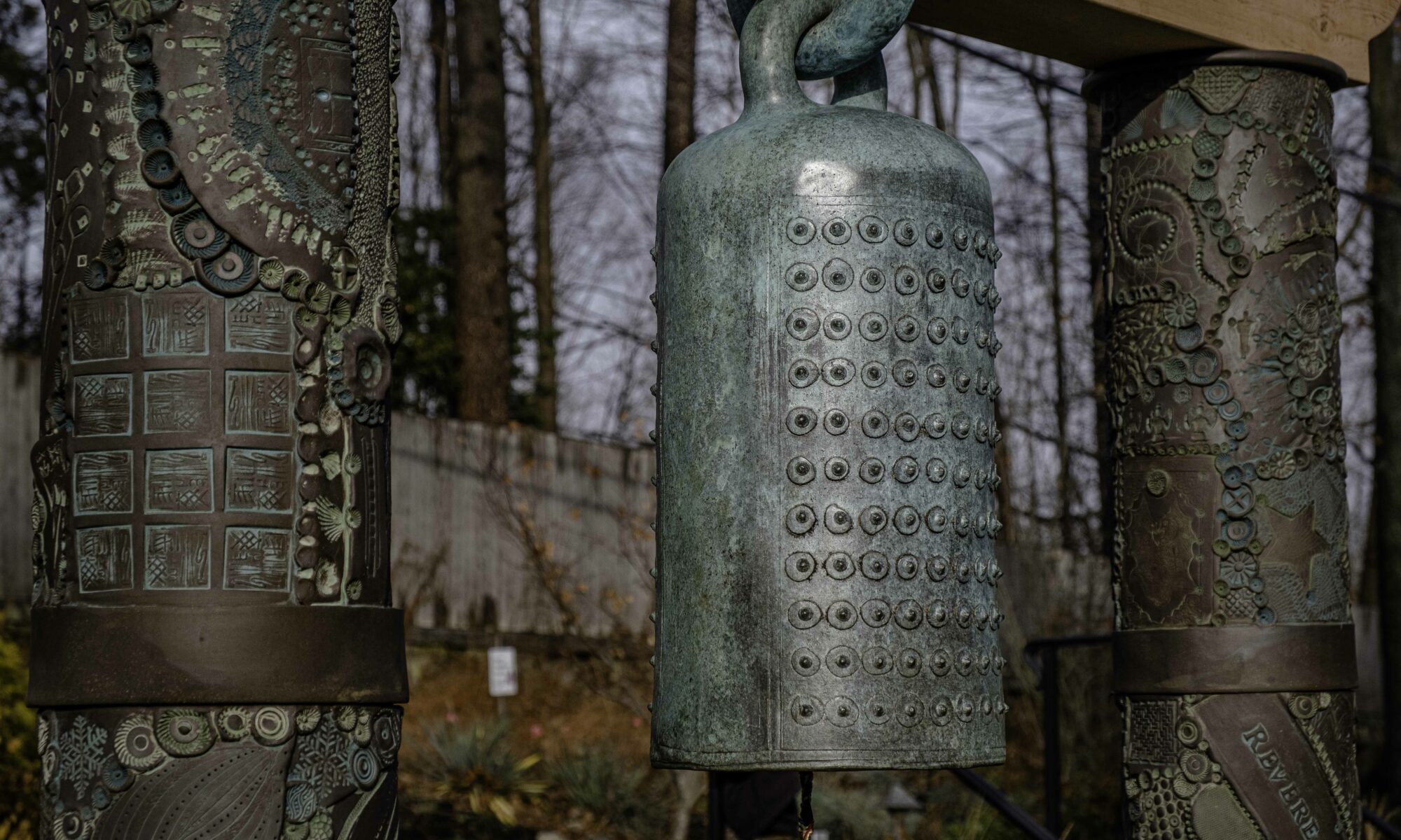 Closeup of the top of the bronze labyrinth bell, suspended between two embellished clay columns