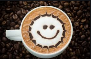 Cup of coffee sitting on a bed of roasted beans, smiley face etched into the foam topping